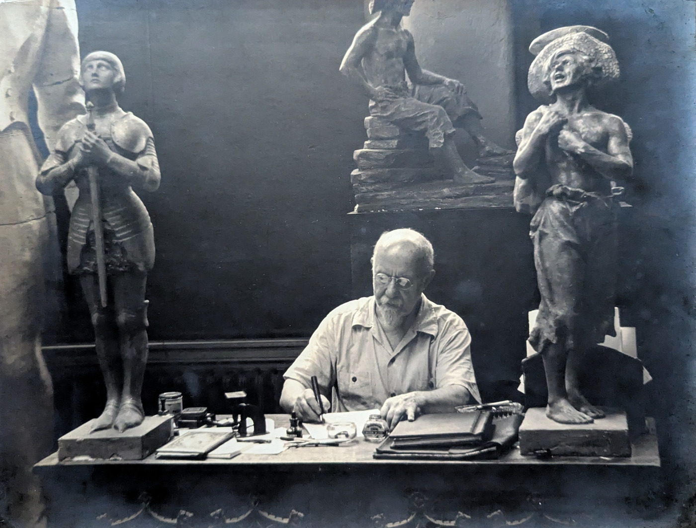 Walter Russell writing at his desk, surrounded by sculptures in his studio.